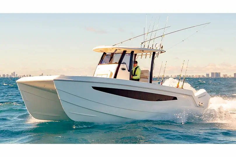 A sleek white motorboat with fishing rods glides through clear blue water, with a person steering at the helm.